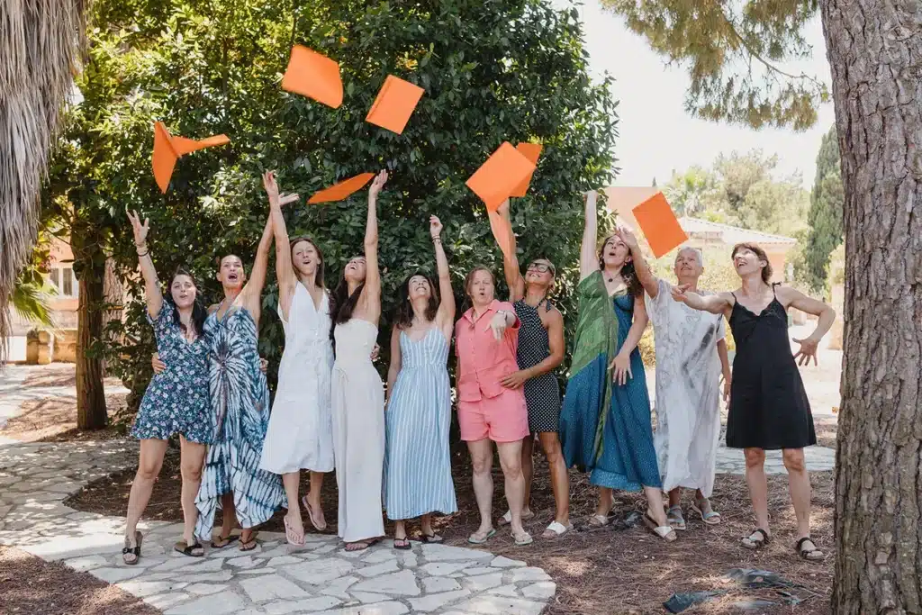 Groupe de femmes joyeuses aux bras levés jetant des feuilles orange en l'air lors d'une célébration en extérieur.