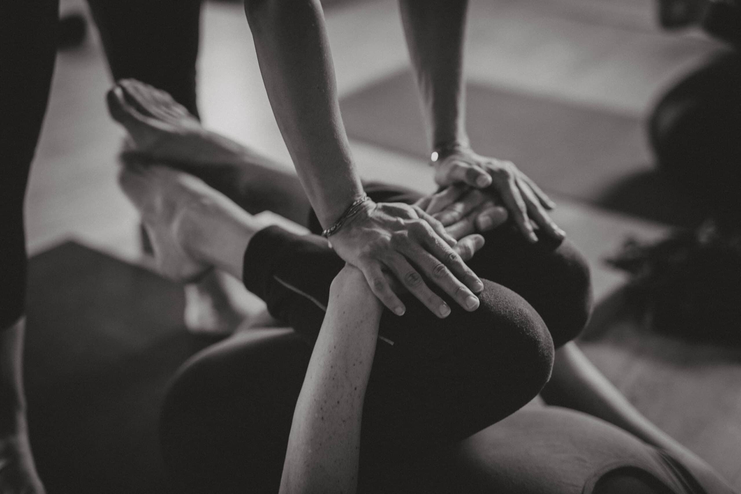 Mains d'un instructeur ajustant la posture de yoga d'une personne allongée, soutien attentif en noir et blanc.